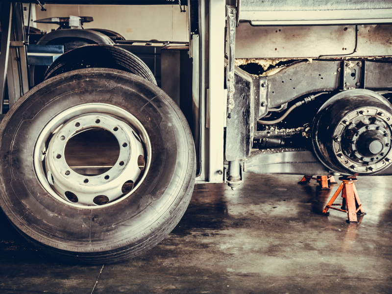 A bus wheel resting against a chassis with a workshop in the background.